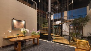 A modern interior with a wooden reception desk, a large black column, a staircase, and indoor plants. - Oceanfront Galle by ICC (Galle)