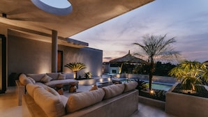 Un espacio exterior moderno con una zona de estar integrada, piscina y una estructura con techo de paja.