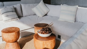 Una sala moderna con un sofá de color claro, dos mesas auxiliares de madera y un cuenco con objetos decorativos sobre una de ellas.