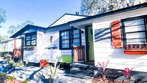 A row of single-story houses with a front porch, a green door, and a window with a red shutter.