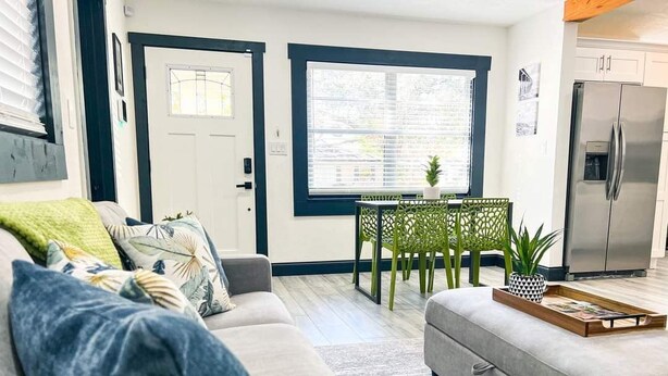A living room with a sofa, a dining table with chairs, a kitchen area with a refrigerator, and a door leading outside.