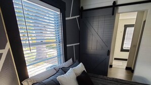 A modern bedroom with a bed, pillows, a bedside lamp, and a window with blinds.