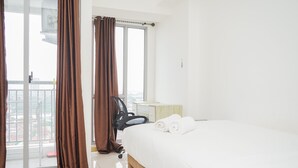 A hotel room with a bed, a chair, a desk, and a window with curtains. - Nice And Comfy Studio Apartment At M-Town Residence (Gading Serpong)