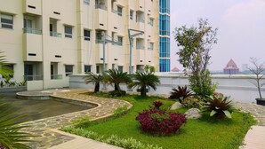 A modern hotel with a pool, surrounded by well-maintained gardens and a view of a distant building. - Simply Clean And Cozy 1Br With Sofabed At Atlanta Residence Apartment (Depok)