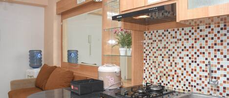 Cocina compacta con estufa a gas, lavamanos y microondas. Cuenta con dispensador de agua y una pequeña zona de estar con una silla y una mesa.