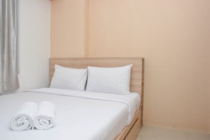 Un lit bien fait, avec du linge de lit blanc et des oreillers, une tête de lit en bois et un mur sobre en arrière-plan.