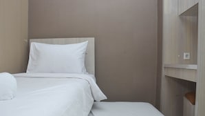 Ein ordentlich bezogenes Bett mit weißer Bettwäsche und Kissen, ein Holz-Kopfbrett und eine kleine Holzkommode mit einem braunen Sitzkissen.