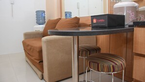 Ein kompakter Wohnraum mit Küchenzeile, einer Couch, zwei gestreiften Sesseln und einer Kaffeemaschine auf einem Glastisch.