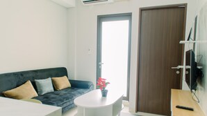A modern living room with a dark grey sofa, a white coffee table, and a wooden side table with a remote control. - Elegant And Comfy 2Br Transpark Bintaro Apartment (South Tangerang)