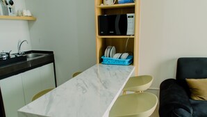 A compact kitchen with a marble countertop, a microwave, and a blue dish rack. There is a black sofa and a small table with chairs. - Elegant And Comfy 2Br Transpark Bintaro Apartment (South Tangerang)