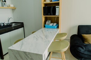 Eine kleine Küche mit Marmorarbeitsplatte, einer Mikrowelle und einem blauen Geschirrregal. Es gibt ein schwarzes Sofa und einen kleinen Tisch mit Stühlen.