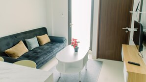 A modern living room with a dark grey sofa, a white coffee table with a red flower, and a wooden side table with a remote control. - Elegant And Comfy 2Br Transpark Bintaro Apartment (South Tangerang)