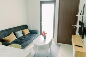 A modern living room with a dark grey sofa, a white coffee table with a red flower, and a wooden side table with a remote control.