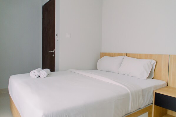A neatly made bed with white linens and two rolled towels, a wooden headboard, and a small bedside table with a black surface.