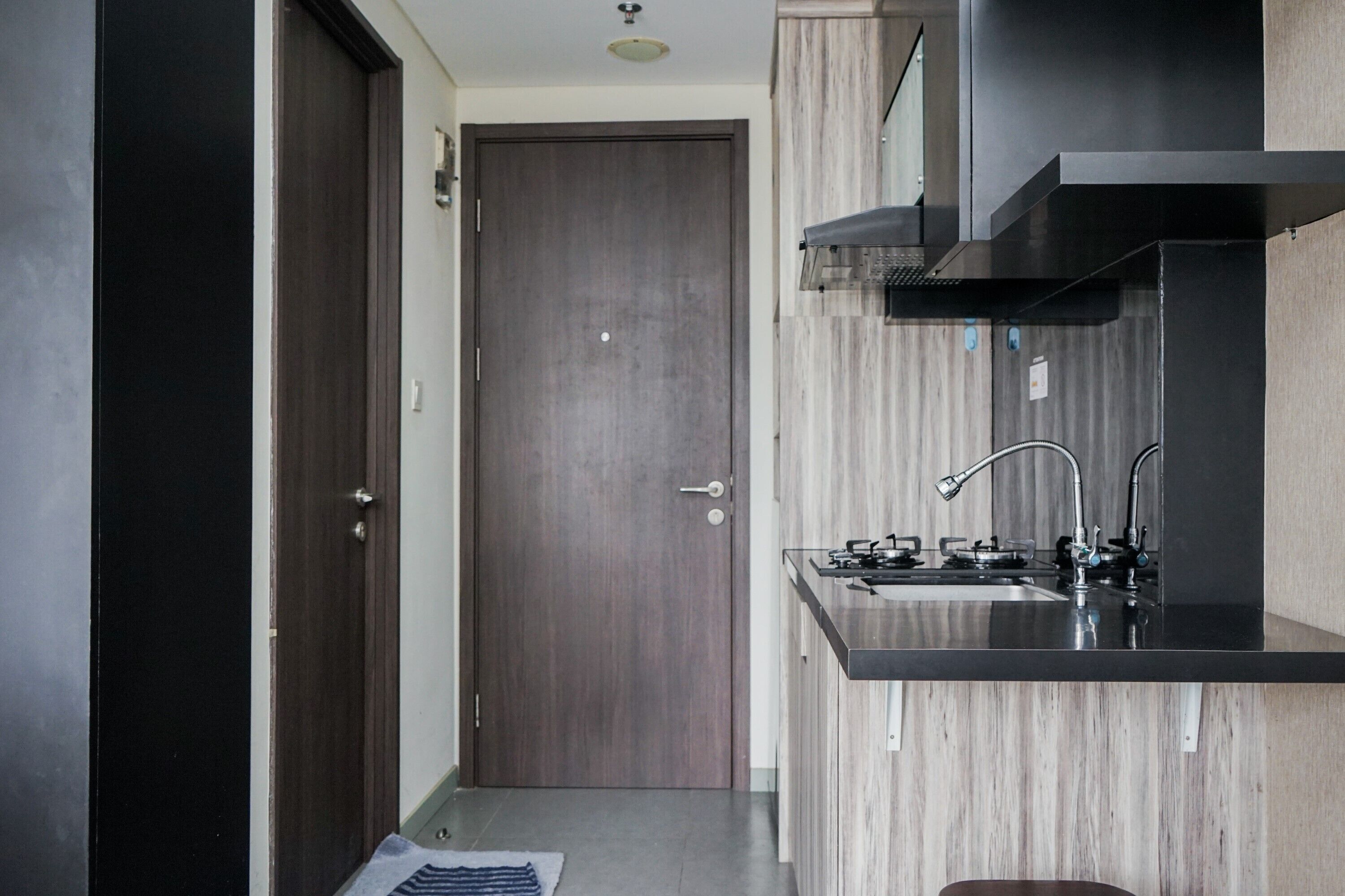 Une cuisine moderne avec une porte en bois foncé, un évier en acier inoxydable et un plan de travail noir.