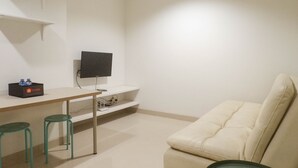 A minimalist room with a white sofa, a small table with a flat-screen TV, and two green stools. - Exclusive 1Br At Apartment Praxis (Surabaya)