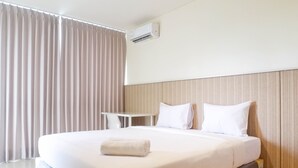 A hotel room with a large bed, white bedding, a small table, and a window with curtains. - Exclusive 1Br At Apartment Praxis (Surabaya)