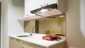 A modern kitchen with a white countertop, stainless steel sink, and a red portable heater. - Exclusive 1Br At Apartment Praxis (Surabaya)