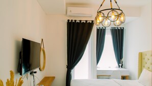 A hotel room with a bed, a desk, a television, and an air conditioning unit. - Cozy Stay Studio Apartment At B Residence Near Aeon Mall (Pagedangan)