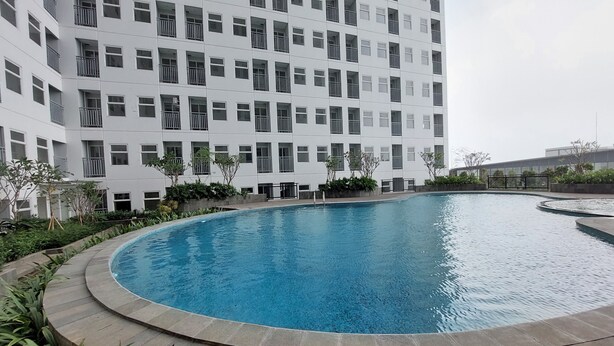 Un edificio moderno con área de piscina, que presenta una piscina circular con borde de piedra y abundante vegetación.