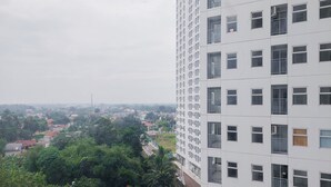 Un edificio de gran altura con varios pisos y balcones, rodeado de vegetación y otros edificios al fondo.