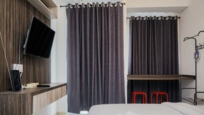 Habitación de hotel moderna con una cama, un televisor montado en una pared de madera, un escritorio con televisor de pantalla plana y un taburete rojo.
