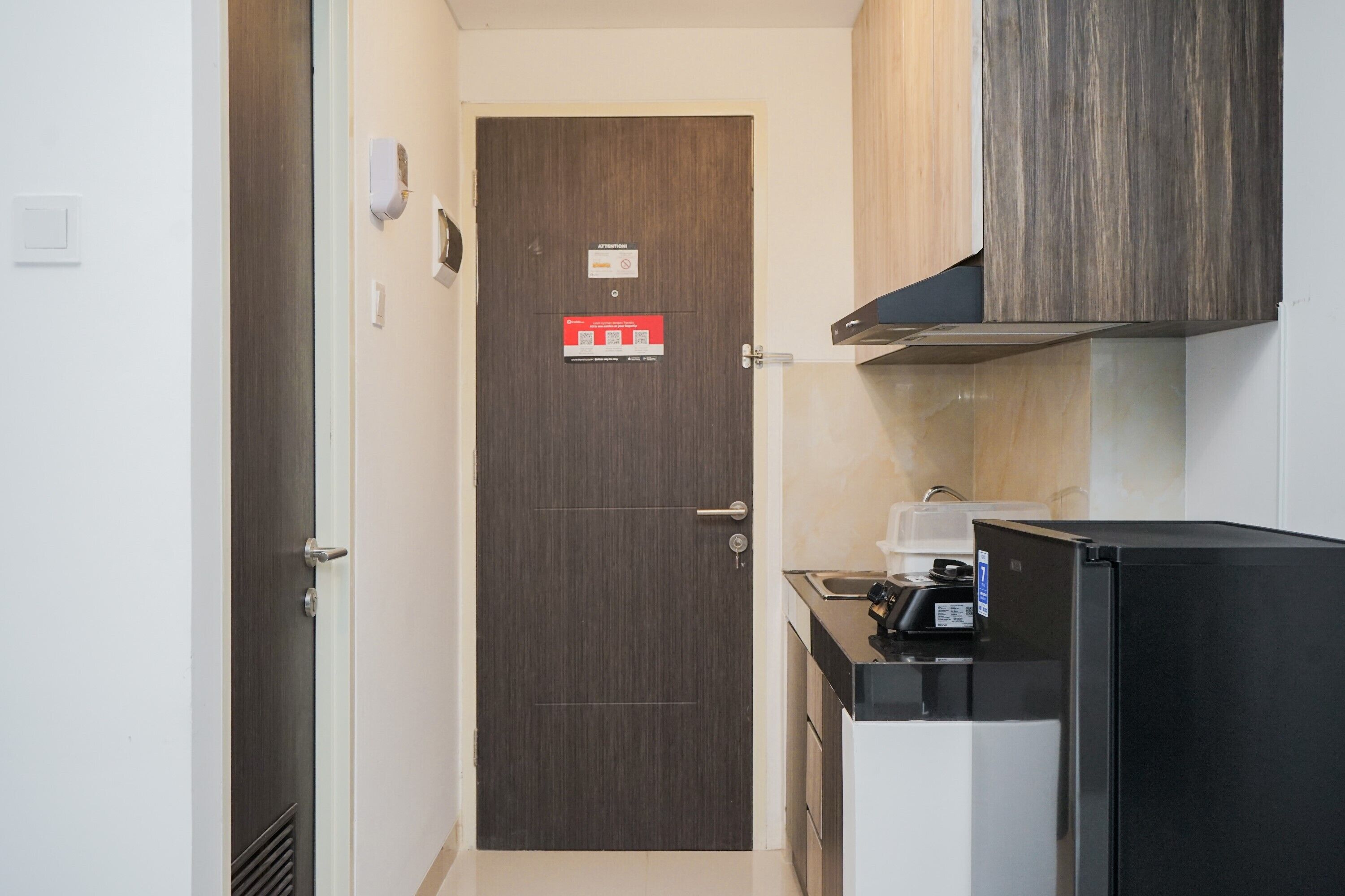 A compact kitchen with a dark wooden door, a black refrigerator, and a countertop with a sink and a coffee machine.