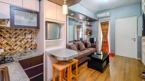 A compact living space with a kitchenette, a sofa, a coffee table, and a television. - Modern Furnished 3Br At Springlake Summarecon Bekasi Apartment (Bekasi)