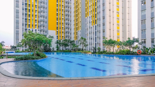 A swimming pool surrounded by greenery and tall residential buildings with balconies. - Modern Furnished 3Br At Springlake Summarecon Bekasi Apartment (Bekasi)