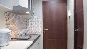 A kitchen with a white countertop, a coffee maker, a toaster, and a brown door. - Comfy Studio Room At Taman Melati Jatinangor (Hegarmanah)