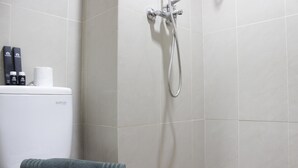 A bathroom with a toilet, a shower, and a towel on the seat. - Comfy Studio Room At Taman Melati Jatinangor (Hegarmanah)