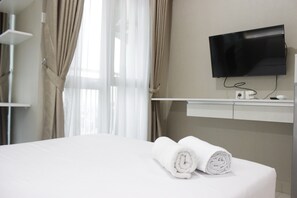 Ein Hotelzimmer mit einem Bett, einem an der Wand montierten Fernseher und einem Fenster mit Vorhängen.
