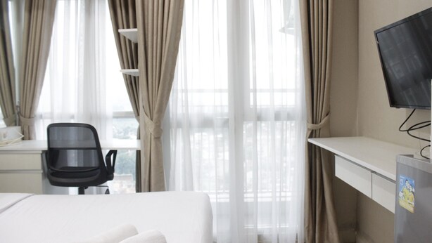 A hotel room with a bed, a desk, a chair, and a TV. - Comfy Studio Room At Taman Melati Jatinangor (Hegarmanah)