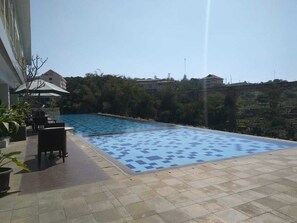 Ein Pool mit einer gefliesten Terrasse, umgeben von Topfpflanzen und Gartenmöbeln.