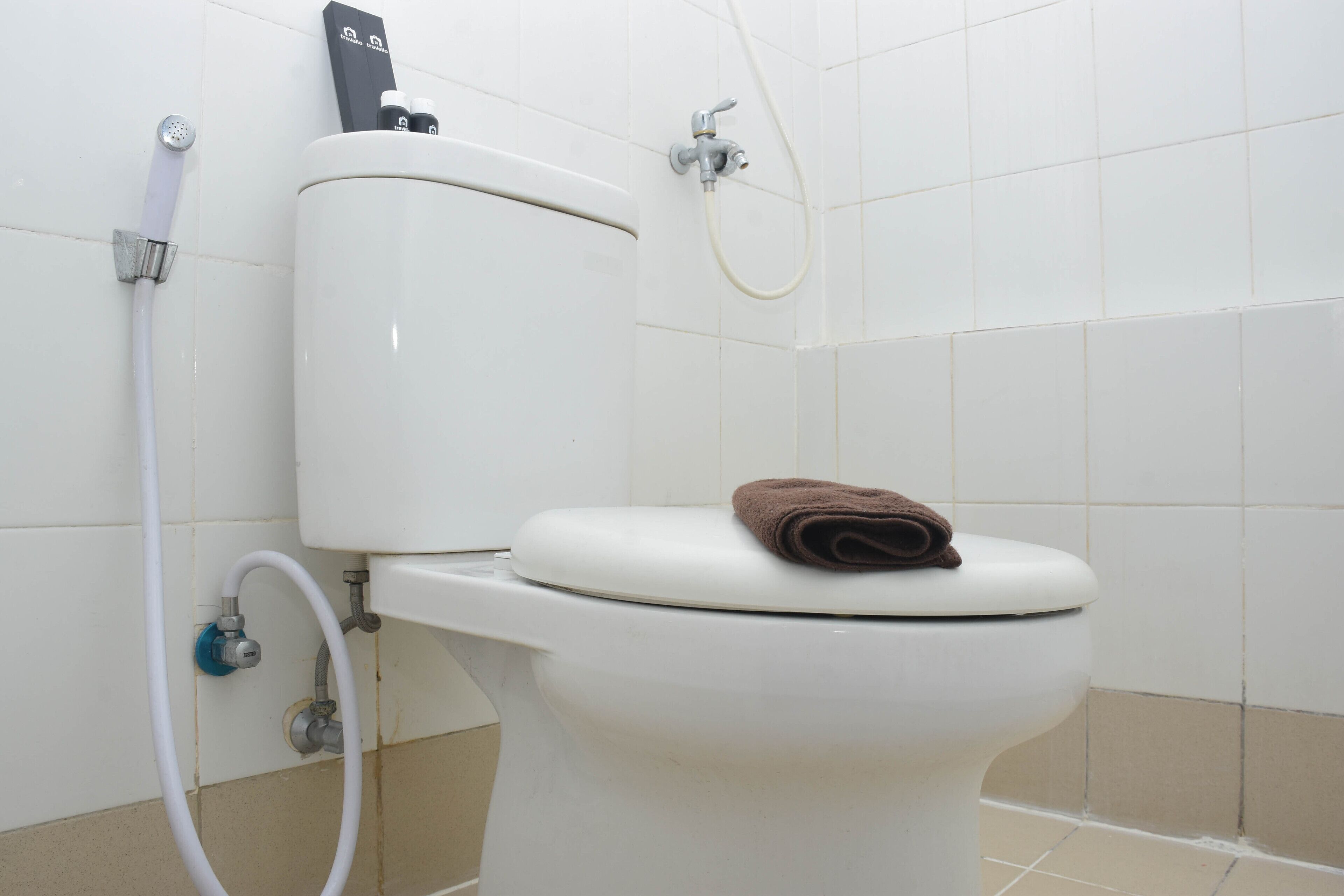 A white toilet with a brown towel on the seat, a bidet attachment, and a handheld showerhead.