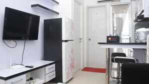 Una moderna camera d'albergo con schermo piatto, frigorifero, angolo cottura e salottino con sedia e tavolo.