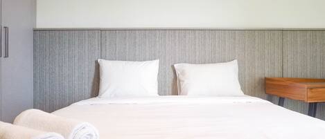 A neatly made bed with white linens and pillows, a wooden nightstand, and a grey headboard.
