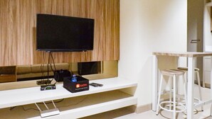 A modern living area with a flat-screen TV mounted on a wooden panel wall, a white entertainment unit with electronic devices, and a white bar stool.