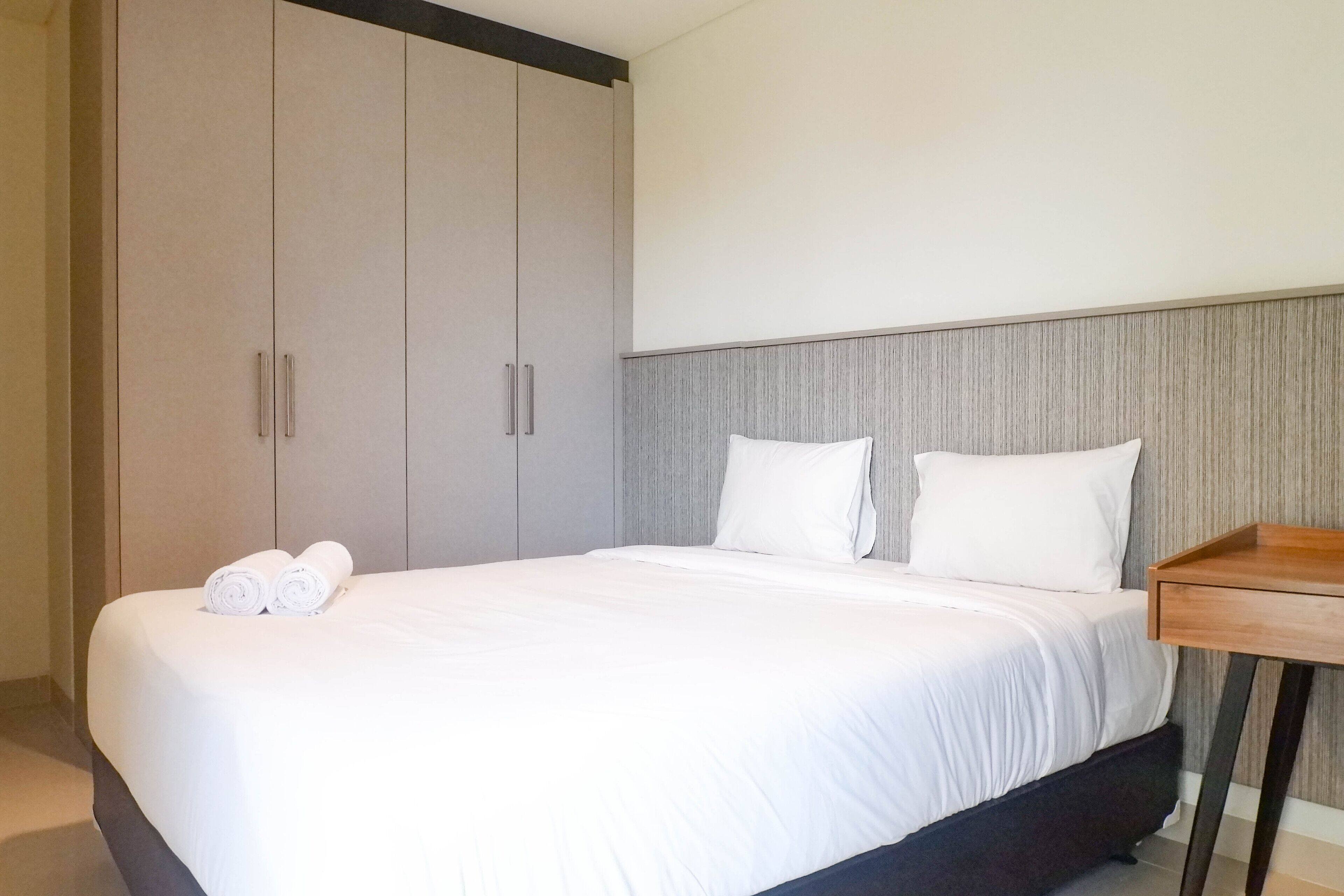 A hotel room with a large bed, two white pillows, and a wooden nightstand.