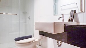 A modern bathroom with a glass shower enclosure, a white toilet, and a vanity with a mirror and a towel rack.
