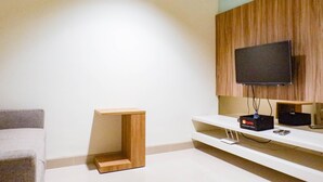 A modern living room with a flat-screen TV mounted on a wooden panel wall, a white entertainment unit below, and a small wooden side table.