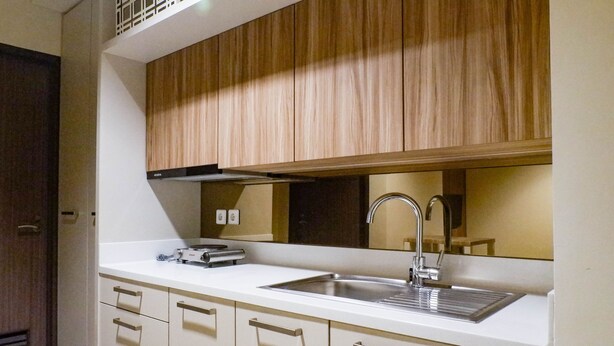 A modern kitchen with a white countertop, stainless steel sink, and wooden cabinets.