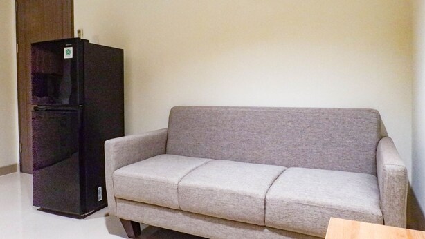 A room with a grey sofa and a black refrigerator. - 1Br Stunning And Cozy Apartment At Praxis (Surabaya)