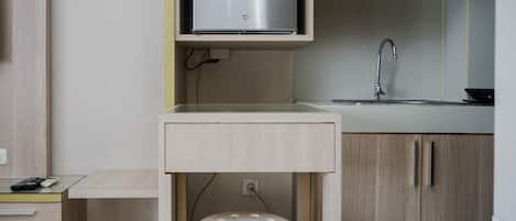 A compact kitchen with a built-in refrigerator, a sink, and a small stool.