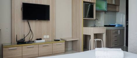 A hotel room with a bed, a TV mounted on the wall, a desk with a sink, and a small stool.