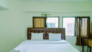 Une chambre d’hôtel avec un grand lit, deux oreillers, une tête de lit en bois, une fenêtre avec des rideaux et une chaise près de la fenêtre.