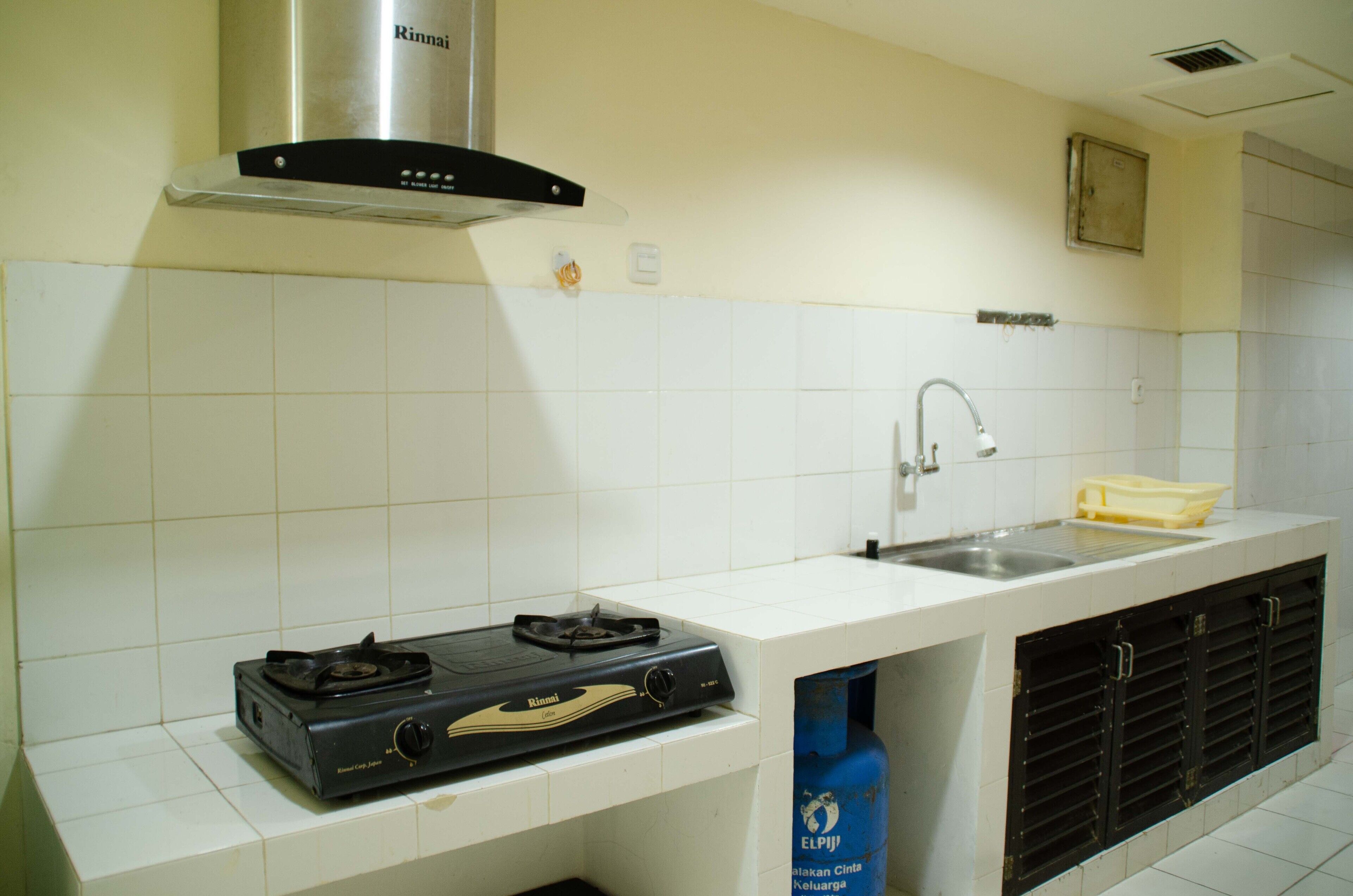 A kitchen with white tiles, a gas stove, a sink, and a ventilation hood.
