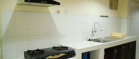 Una cocina con azulejos blancos, estufa a gas, lavamanos y campana extractora.