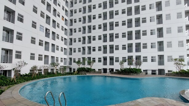 A modern building with a central swimming pool surrounded by a wooden deck. - Comfy And Minimalist Studio Room At Serpong Garden Apartment (Cisauk)