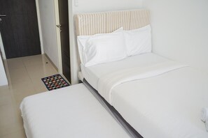 A neatly made bed with white bedding, a striped headboard, and a small checkered rug on the floor. - Comfy And Minimalist Studio Room At Serpong Garden Apartment (Cisauk)